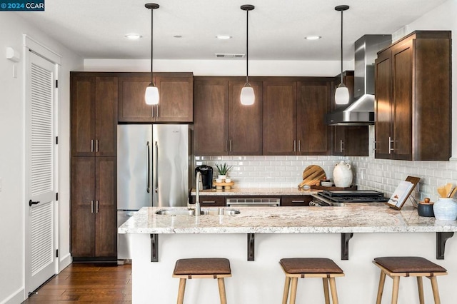 kitchen featuring decorative light fixtures, backsplash, wall chimney range hood, stove, and light stone counters