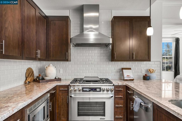 kitchen with light stone countertops, backsplash, appliances with stainless steel finishes, and wall chimney exhaust hood