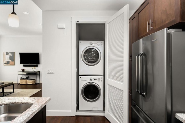 clothes washing area with stacked washer / drying machine and dark wood-type flooring