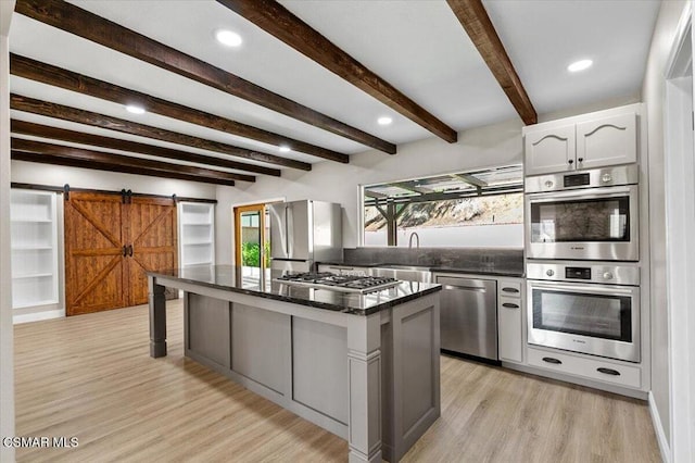 kitchen with white cabinets, a barn door, beam ceiling, appliances with stainless steel finishes, and a kitchen island