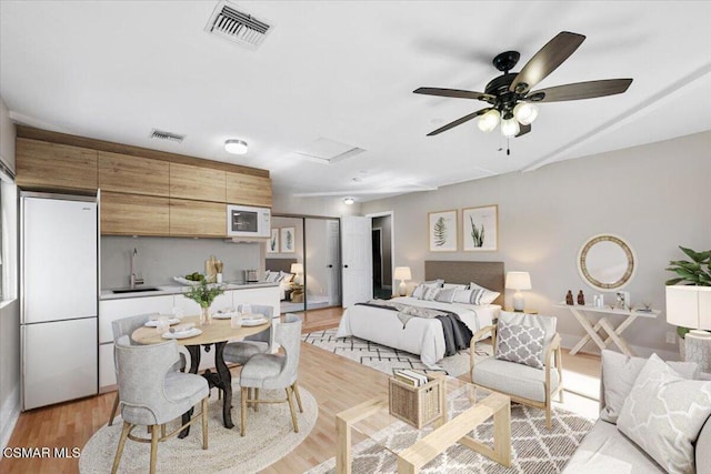 bedroom featuring light hardwood / wood-style floors, ceiling fan, sink, white fridge, and a closet