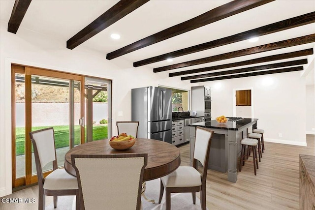 dining room with light hardwood / wood-style flooring, beamed ceiling, and sink