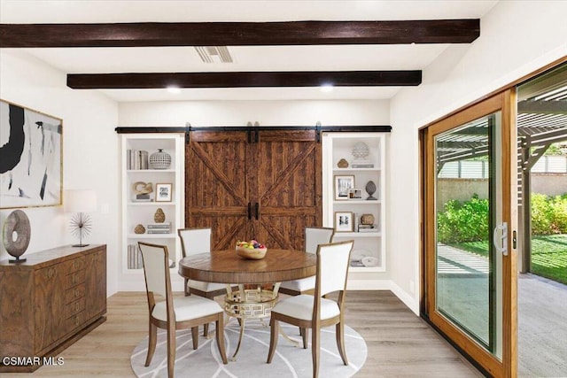 dining area with a barn door, beam ceiling, and light hardwood / wood-style flooring