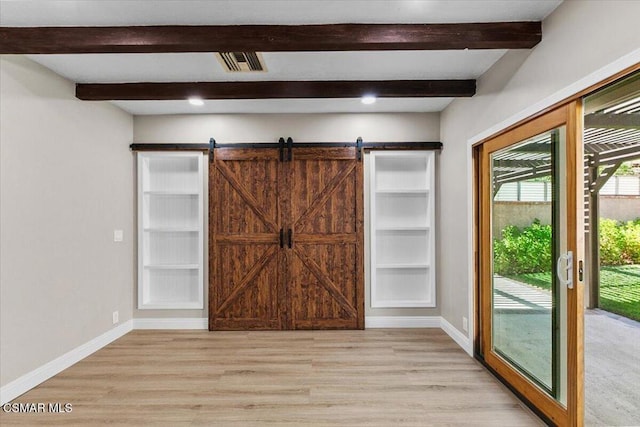 interior space featuring beam ceiling, a barn door, and light hardwood / wood-style flooring