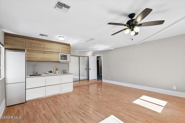 kitchen featuring white appliances, white cabinets, sink, ceiling fan, and light wood-type flooring