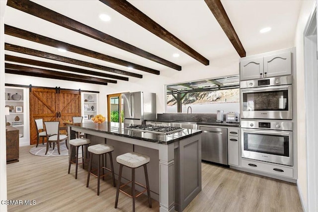 kitchen with white cabinets, stainless steel appliances, a barn door, beamed ceiling, and a kitchen island