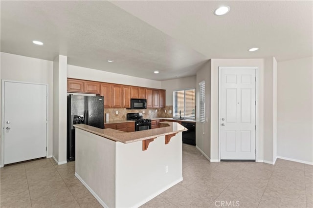 kitchen with black appliances, a kitchen island, light tile patterned flooring, and a breakfast bar area