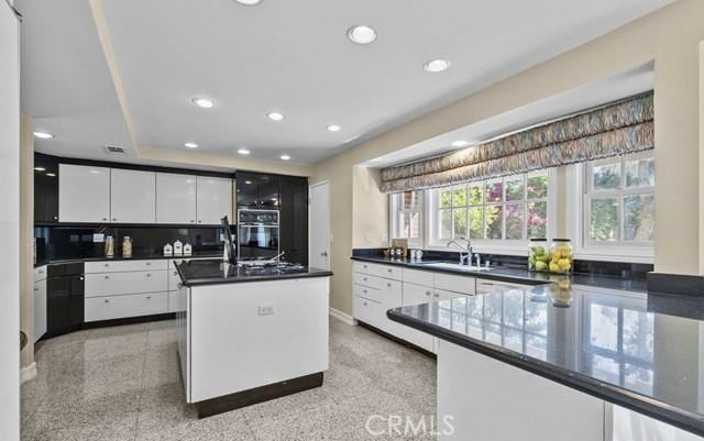 kitchen featuring a kitchen island, decorative backsplash, sink, white cabinetry, and black double oven