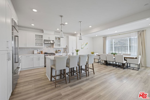 kitchen with white cabinetry, light hardwood / wood-style flooring, an island with sink, decorative light fixtures, and appliances with stainless steel finishes