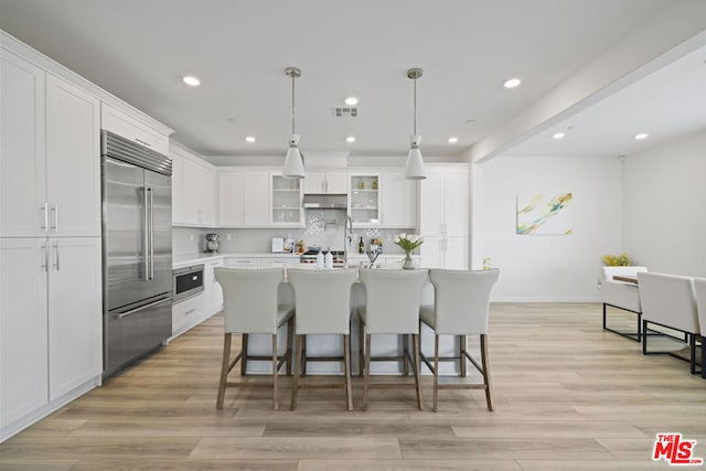 kitchen featuring a kitchen island with sink, white cabinets, light wood-type flooring, appliances with stainless steel finishes, and decorative light fixtures