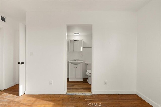 unfurnished bedroom with hardwood / wood-style floors, ensuite bath, and sink