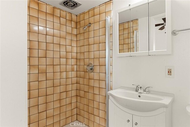 bathroom featuring ceiling fan, tiled shower, and vanity