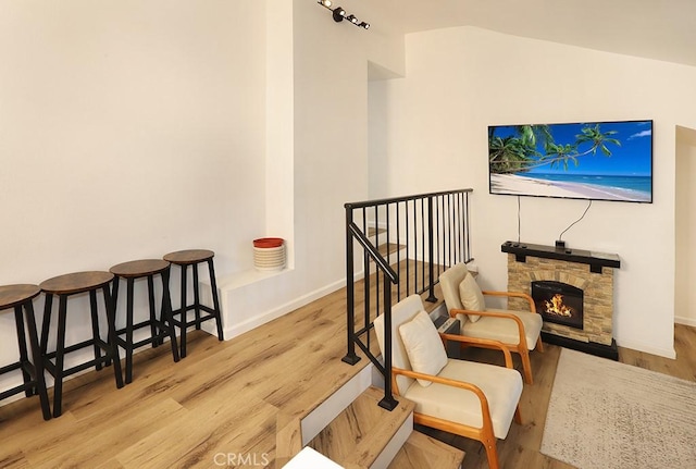 sitting room with a stone fireplace, light hardwood / wood-style flooring, and lofted ceiling