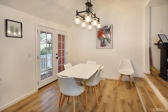 dining area with a chandelier, vaulted ceiling, french doors, and light hardwood / wood-style flooring