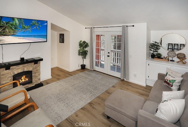 living room with light hardwood / wood-style floors, vaulted ceiling, a fireplace, and french doors