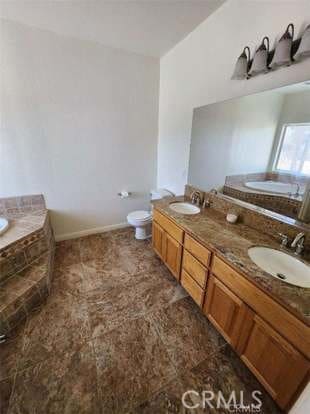 bathroom with tiled tub, vanity, and toilet