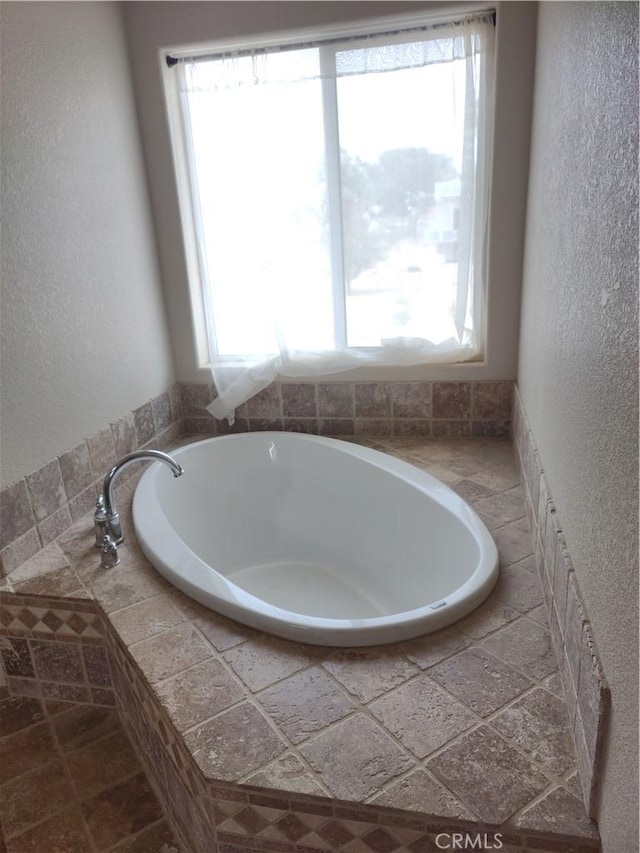 bathroom featuring a healthy amount of sunlight and tiled bath