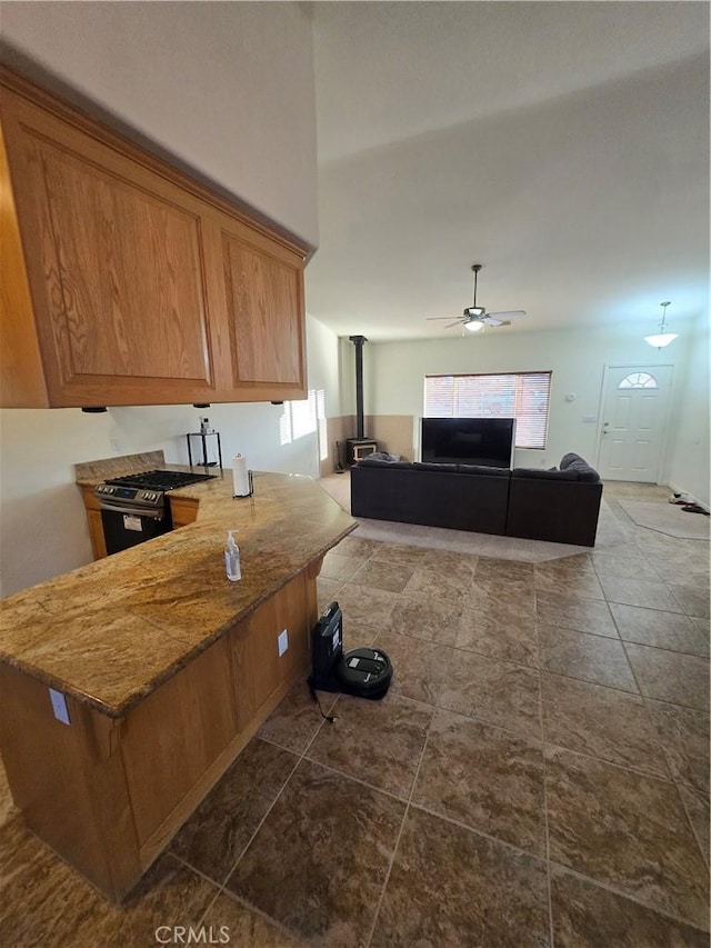 kitchen featuring gas range, kitchen peninsula, ceiling fan, and a wood stove