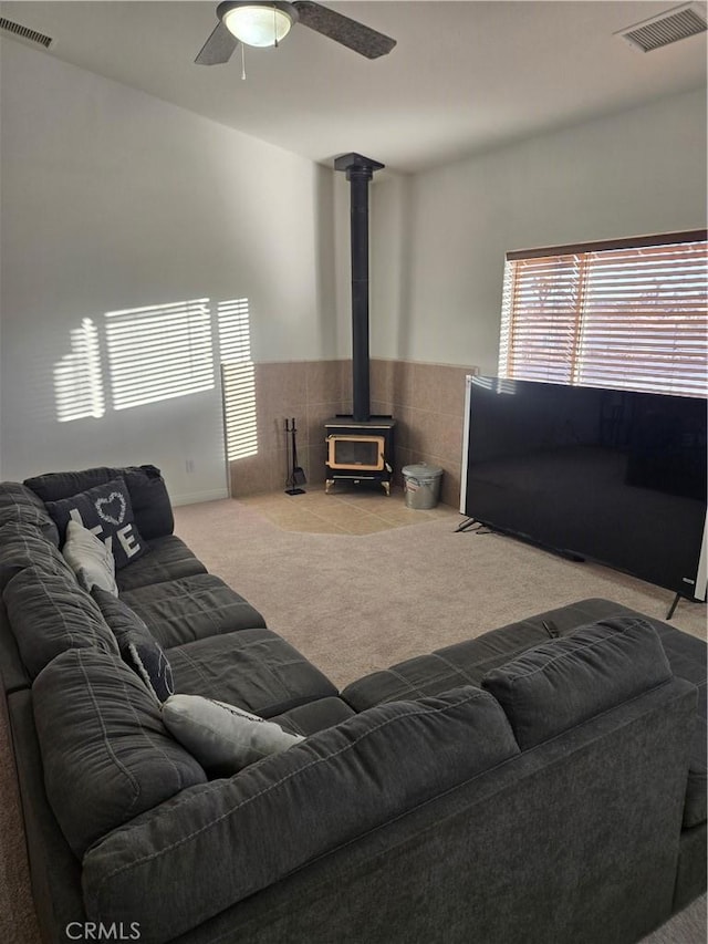 carpeted living room with a wood stove and ceiling fan