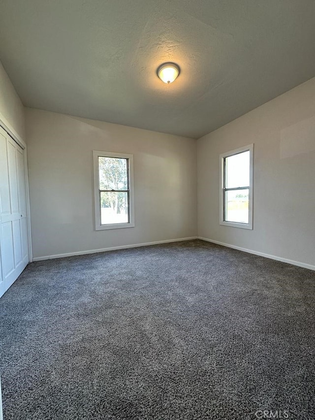 empty room with dark colored carpet, a textured ceiling, and a wealth of natural light