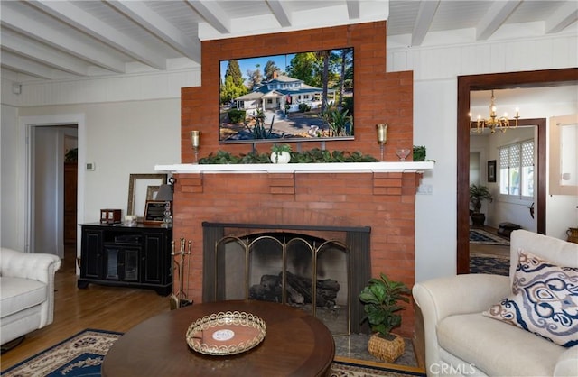 living room with hardwood / wood-style flooring, beamed ceiling, a notable chandelier, and a brick fireplace