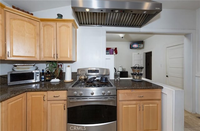 kitchen featuring wall chimney range hood, dark stone countertops, light brown cabinetry, light tile patterned flooring, and stainless steel range with gas stovetop