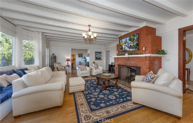 living room featuring beam ceiling, light wood-type flooring, a fireplace, and a chandelier