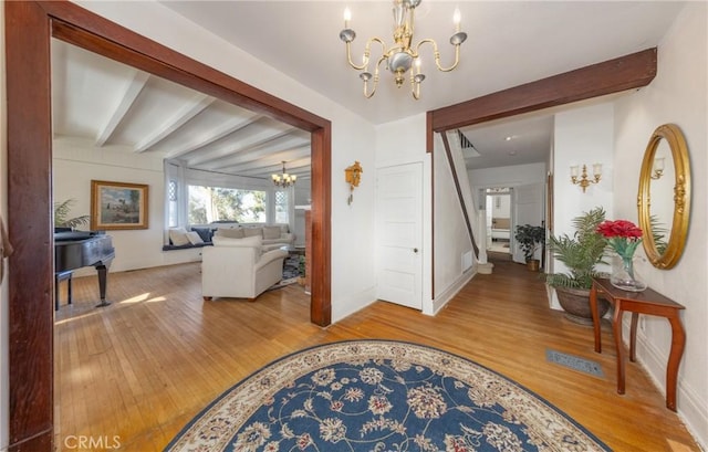 foyer entrance featuring beam ceiling, wood-type flooring, and an inviting chandelier