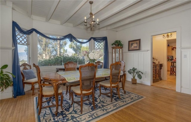 dining space with hardwood / wood-style floors, beam ceiling, and an inviting chandelier