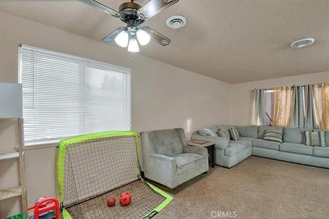 living area with a ceiling fan, light colored carpet, visible vents, and a textured ceiling