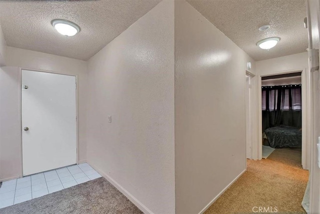 hall with light carpet, baseboards, and a textured ceiling