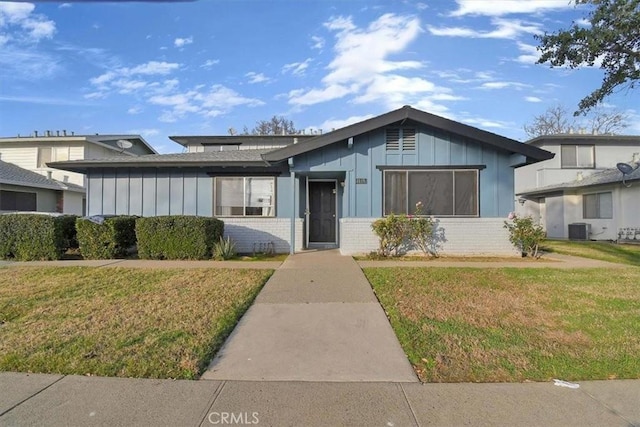 view of front facade featuring board and batten siding, brick siding, a front lawn, and central air condition unit