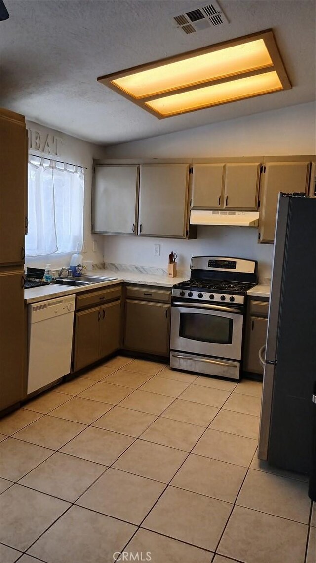 kitchen featuring vaulted ceiling, sink, appliances with stainless steel finishes, and light tile patterned flooring