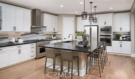 kitchen with a kitchen island with sink, sink, wall chimney exhaust hood, light wood-type flooring, and stainless steel appliances