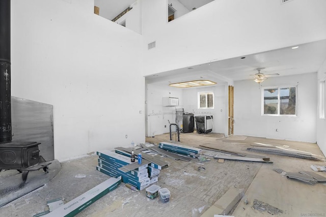 living room with ceiling fan, a towering ceiling, and a wood stove