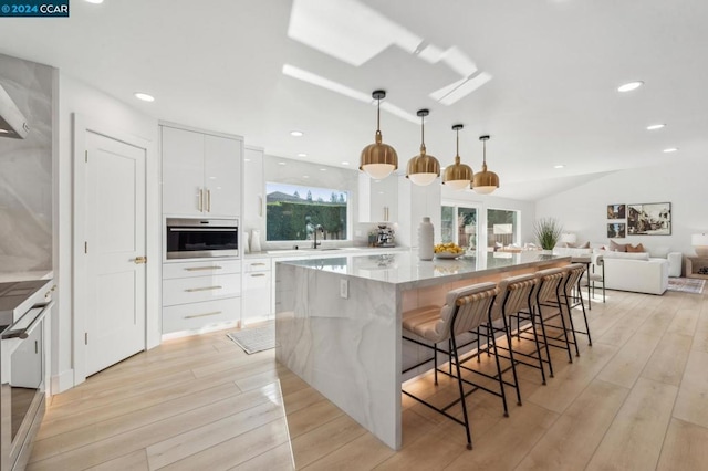 kitchen with a kitchen breakfast bar, a center island, white cabinets, decorative light fixtures, and oven