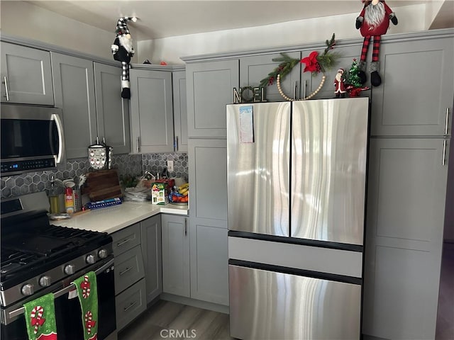 kitchen with gray cabinets, light wood-type flooring, stainless steel appliances, and tasteful backsplash