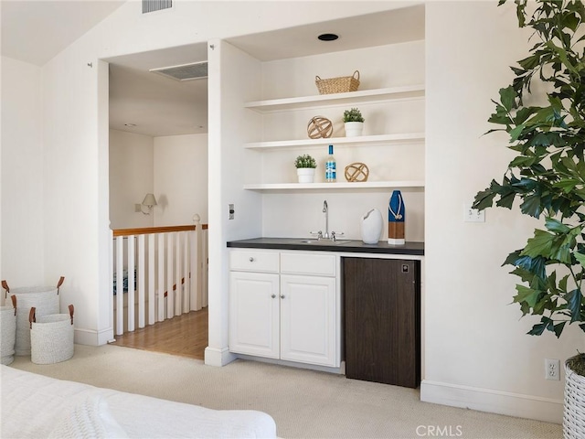 bar with white cabinetry, sink, and light colored carpet