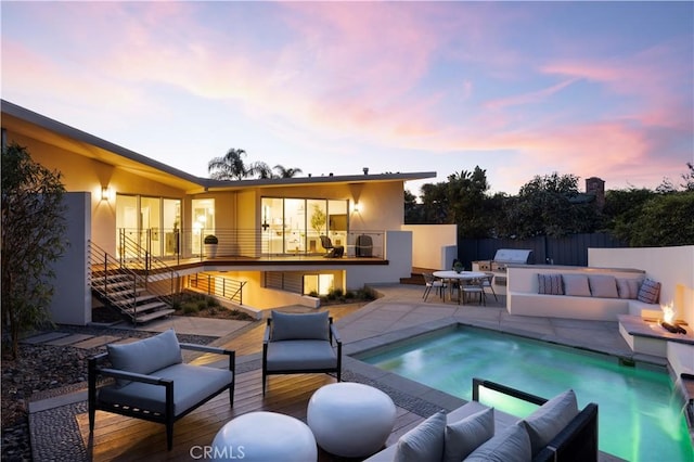 back of house at dusk featuring an outdoor kitchen, a jacuzzi, fence, stairs, and an outdoor living space with a fire pit