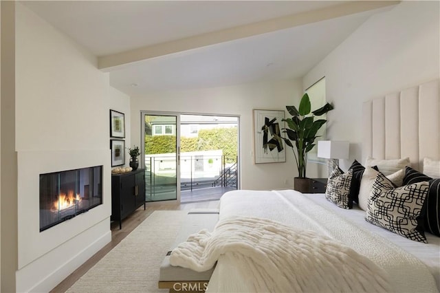 bedroom featuring access to exterior, vaulted ceiling, and a glass covered fireplace