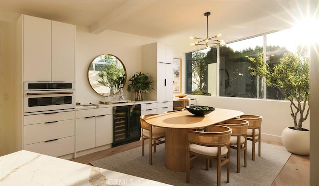 dining room featuring light wood finished floors, beverage cooler, beamed ceiling, and an inviting chandelier