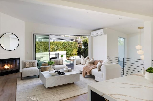 living area featuring an AC wall unit, light wood-type flooring, and a glass covered fireplace