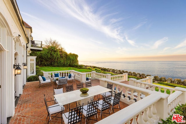 patio terrace at dusk with outdoor lounge area, a balcony, and a water view