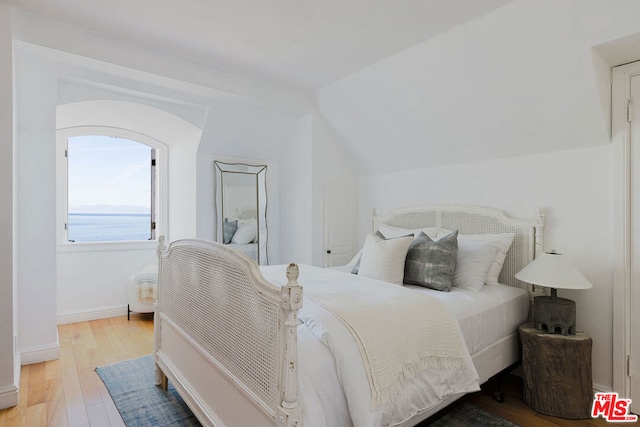 bedroom with light hardwood / wood-style flooring, a water view, and lofted ceiling