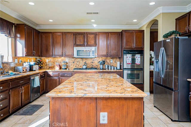 kitchen with backsplash, a kitchen island, light stone countertops, and stainless steel appliances