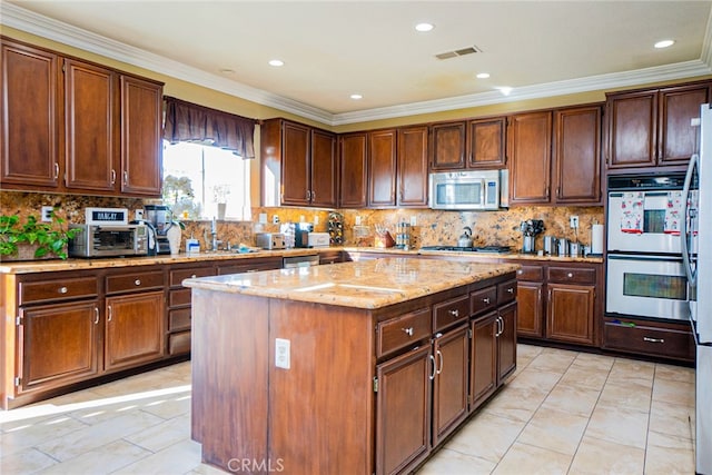 kitchen with appliances with stainless steel finishes, tasteful backsplash, light stone counters, ornamental molding, and a center island