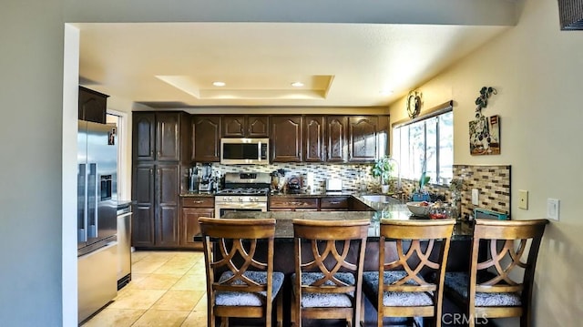 kitchen with stainless steel appliances, kitchen peninsula, a tray ceiling, decorative backsplash, and a breakfast bar