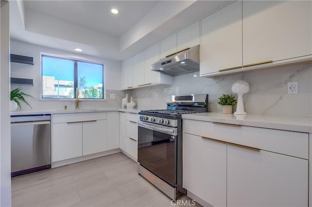 kitchen featuring backsplash, sink, a tray ceiling, white cabinetry, and appliances with stainless steel finishes