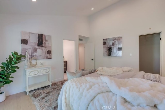 bedroom featuring ensuite bathroom, light hardwood / wood-style flooring, and high vaulted ceiling