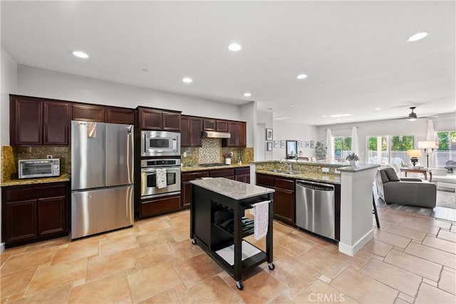 kitchen with kitchen peninsula, ceiling fan, stainless steel appliances, light stone countertops, and decorative backsplash